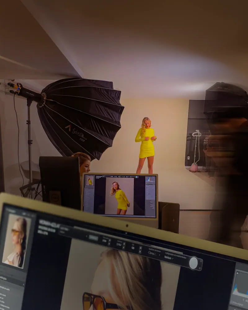 Ensaio de moda no fundo infinito, com a modelo de amarelo, refletor parabólico e a foto aparecendo no monitor
