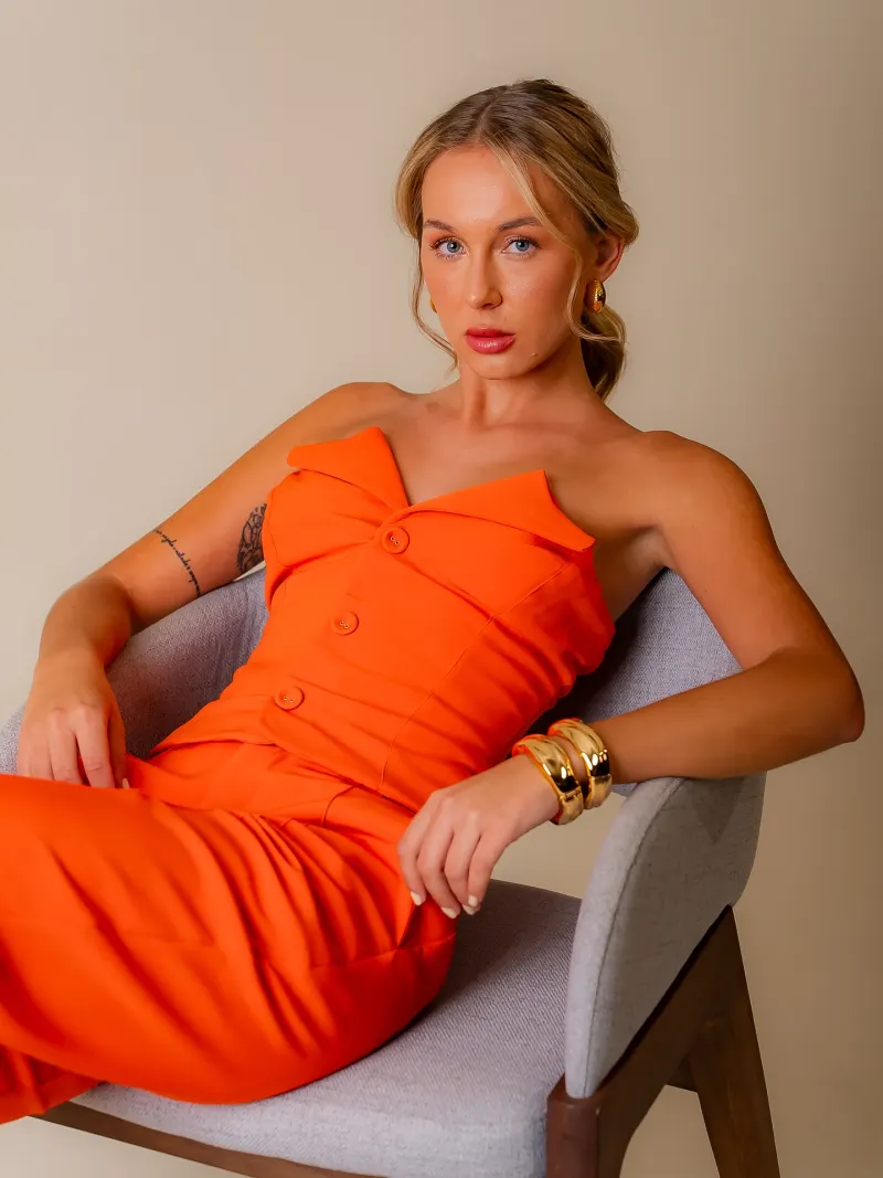 Modelo de vestido laranja sentada em poltrona no estúdio